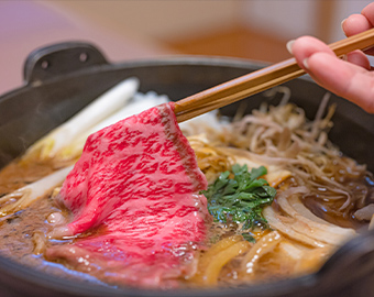 すき焼き鍋から箸で霜降り和牛をつまみ上げる様子の写真